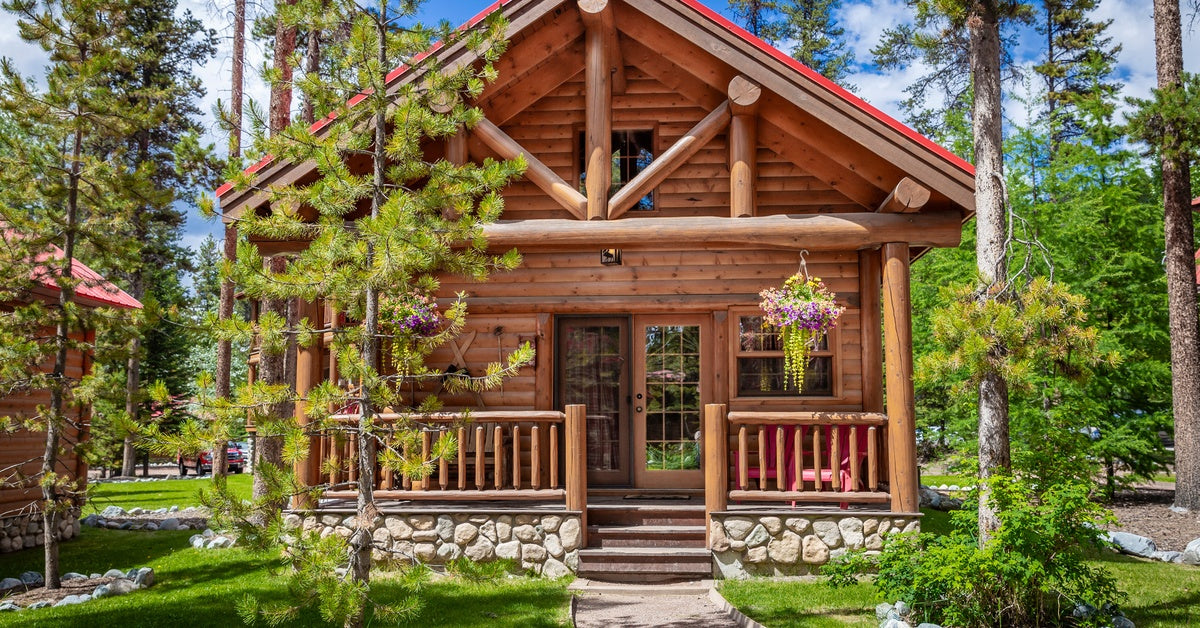 A log cabin with a stone foundation, a cozy front porch, and neat, well-maintained landscaping.