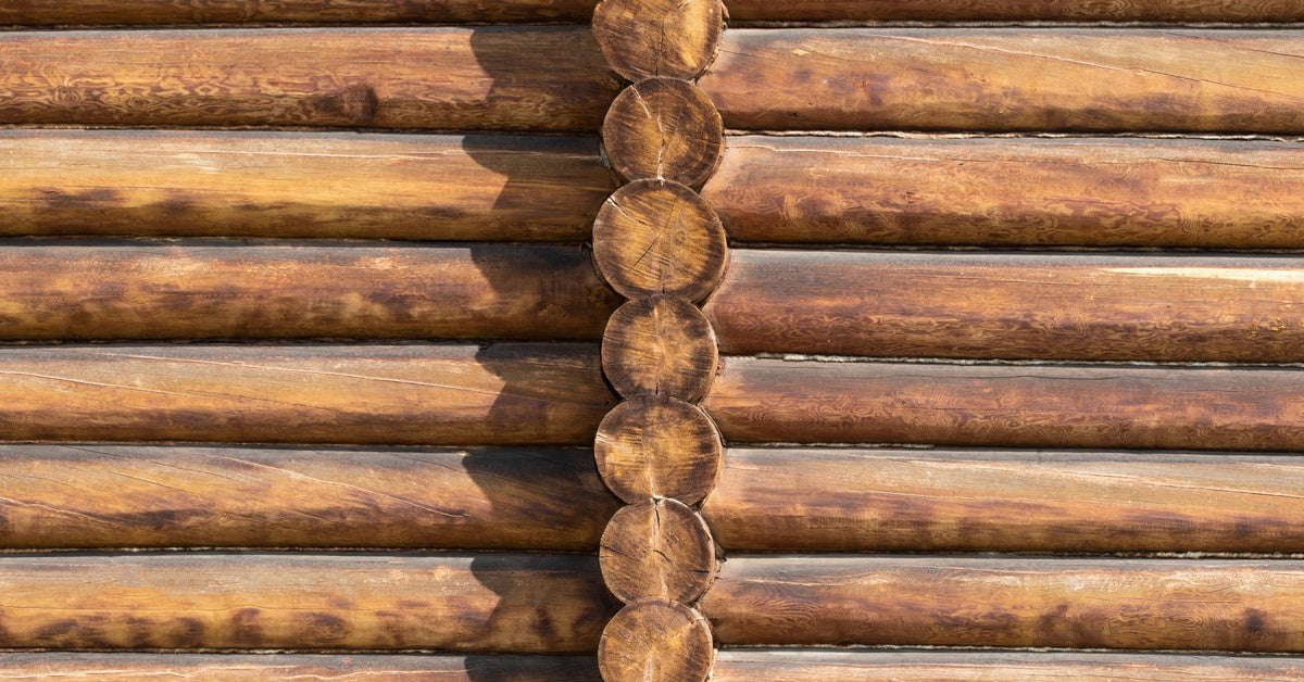 A log cabin with two horizontal rows of logs in a rich mid-brown hue with red undertones, divided by a log row facing inward.