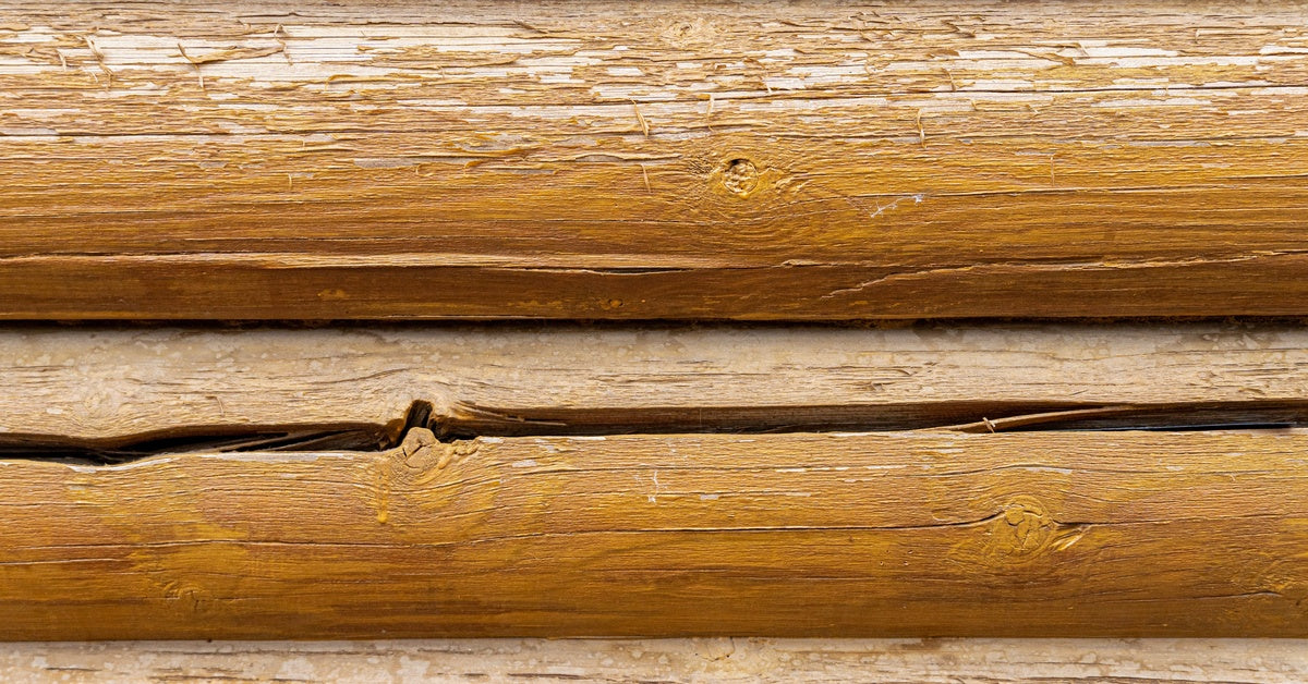 A light orange wooden log, part of a collection on home siding, displaying a long, deep vertical crack.