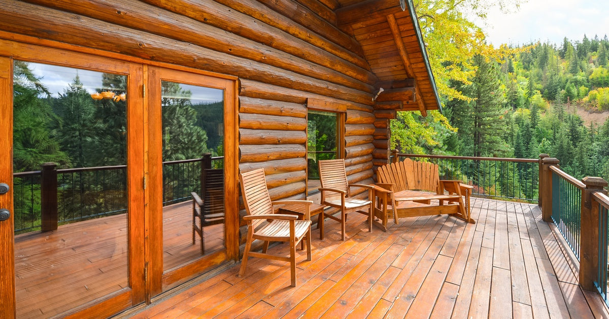 A log home with a deck connected to the house by a sliding glass door, with two chairs and a bench on it.