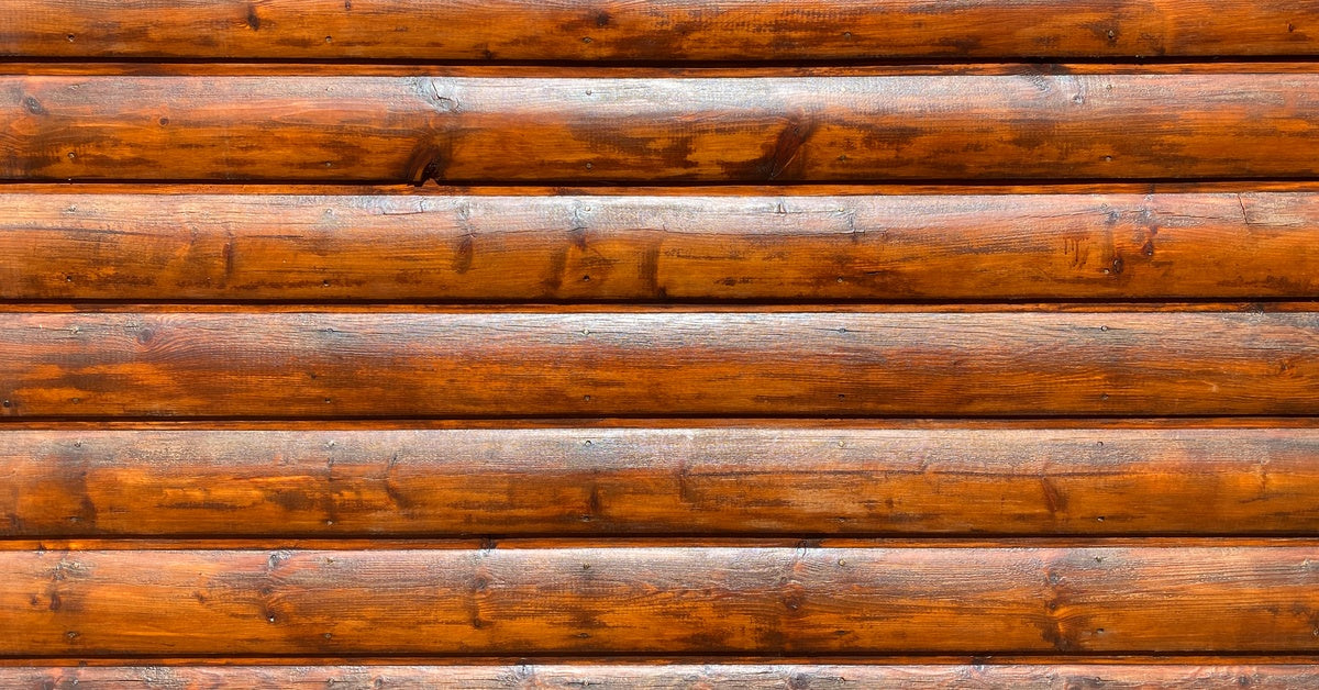 A close-up of a varnished wooden log cabin wall with smooth, shiny surface and visible wood grain texture.